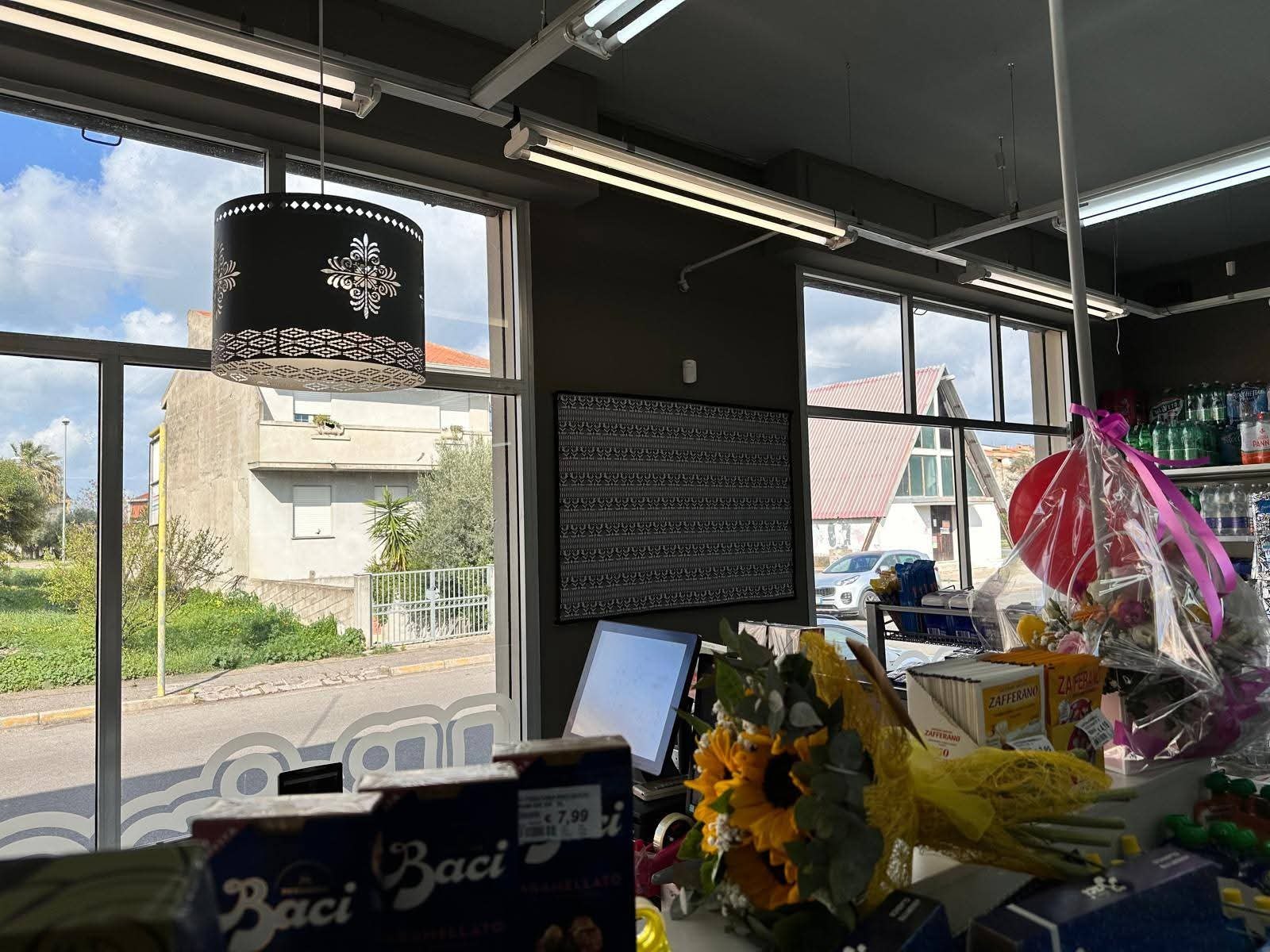 Cassa del Sorriso Market con Baci a 7,99 €, girasoli e lampada nera decorata davanti alle vetrate sulla strada