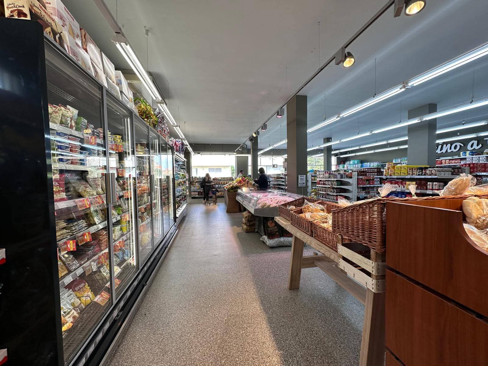 Corsia di Vicino a Te tra frigoriferi a vetri e cesti di vimini col pane, frutta e verdura sul fondo